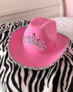 a pink cowboy hat sitting on top of a zebra print bed sheet with a tiara