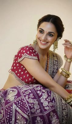 a woman in a red and white sari sitting on the ground with her hand up to her face