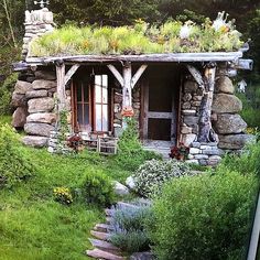 an old log cabin with plants growing on the roof and stairs leading up to it