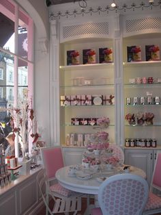 there is a white table and pink chairs in the room with shelves full of teacups