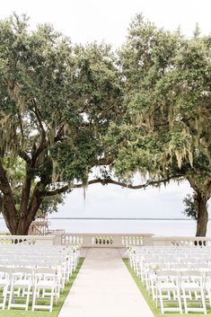 an outdoor ceremony setup with white chairs and trees