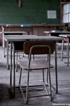 an empty classroom with desks and chairs in the foreground, on which there is a chalkboard