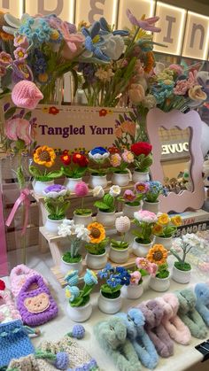 there are many stuffed animals on display at this market table with flowers and plants in pots