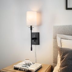 a table with a book and cup on it next to a lamp in a bedroom