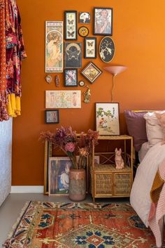 a bedroom with an orange wall and lots of pictures on the wall, including flowers