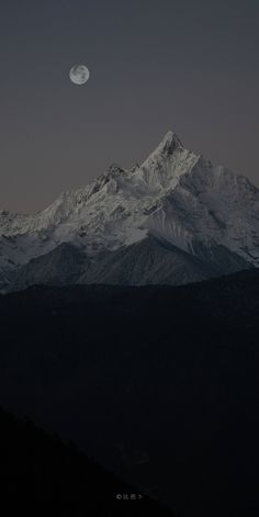 the moon is setting on top of a mountain in the distance, with snow - capped mountains behind it