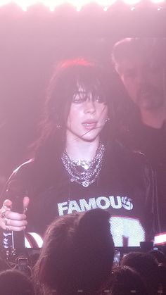 a woman standing in front of a crowd holding a microphone and wearing a t - shirt that says famous