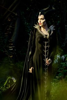 a woman dressed as maleficent stands in the woods with her hands on her hips