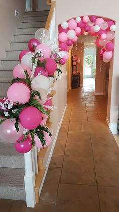 pink and white balloons are hanging from the banisters in this entryway decorated with greenery