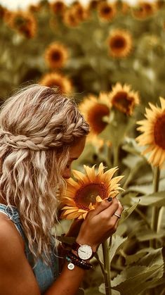 a woman standing in a field of sunflowers with her hands on the flower