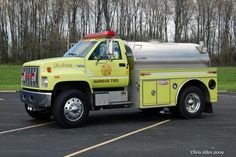 a yellow fire truck is parked in a parking lot with trees and grass behind it