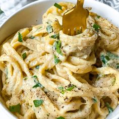 a white bowl filled with pasta covered in sauce and parmesan cheese, topped with a gold fork