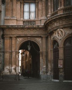 two people are walking down the street in front of an old building with arched doorways