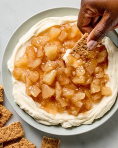 a person dipping some food on top of a white plate next to crackers and crackers