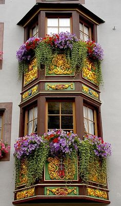 an ornate window box with flowers on the top and bottom, in front of a building