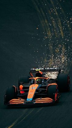 an orange race car driving down the road with fireworks in the air behind it and on top of its wheels