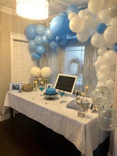 a table topped with balloons and cake next to a white table cloth covered table in front of a window