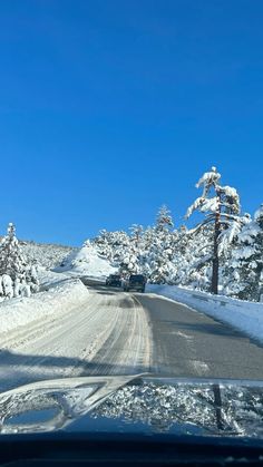 a car driving down a snow covered road in the middle of winter with trees on both sides