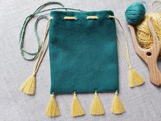 a green bag with yellow tassels next to yarn