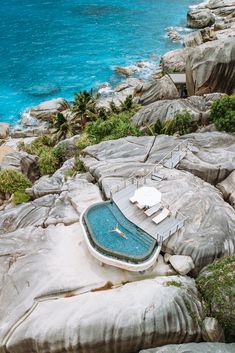 an outdoor swimming pool surrounded by rocks near the water's edge and blue ocean