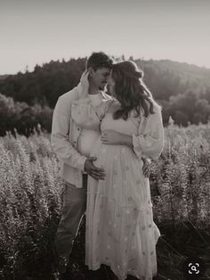 a pregnant couple cuddle in the middle of a field