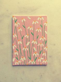 a pink square with daisies on it sitting on top of a table next to a white wall