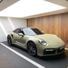 a beige sports car is parked in a parking lot next to a wall with wood paneling