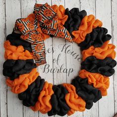 an orange and black halloween wreath with pumpkins on it sitting on a white wooden surface