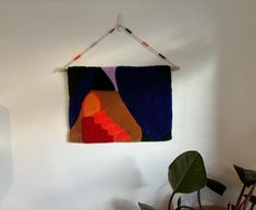 a wall hanging on the side of a white wall next to a potted plant