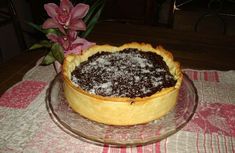 a cake with powdered sugar on top sits on a glass plate next to a pink flower