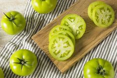 several green tomatoes on a cutting board with one cut in half and the other whole