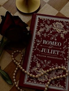 a red book with pearls and a rose on the table next to it is a necklace that reads,'romeo and julia william shakespeare '