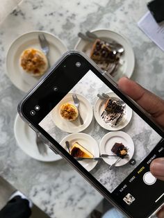 a person holding up a cell phone to take a picture of desserts on plates