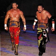 two men in wrestling gear walking down the street with one holding his hand on his hip