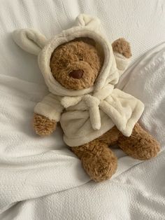 a teddy bear wearing a robe on top of a bed