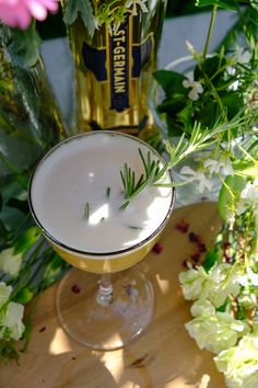 a glass filled with a drink sitting on top of a wooden table next to flowers