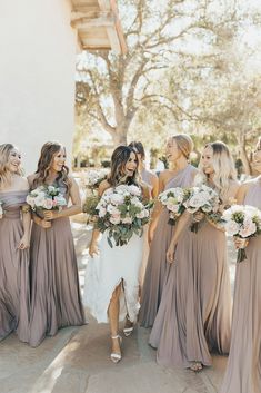 a group of women standing next to each other in front of a white building holding bouquets