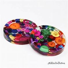 two tins filled with colorful buttons on top of a white surface, next to each other