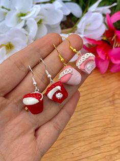 a hand holding three pairs of red and white christmas stocking earrings on it's fingers