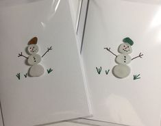 two snowmen made out of paper on top of white envelopes with green trim