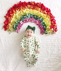 a baby laying on top of a bed next to a rainbow shaped wall paper decoration