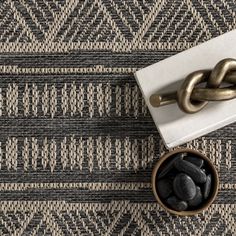 a bowl filled with black rocks next to a metal chain on top of a rug