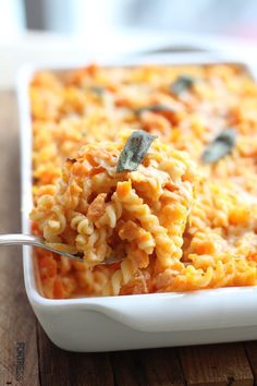 a white dish filled with macaroni and cheese on a wooden table next to a fork