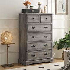 a gray dresser sitting in a room next to a chair and potted plant on top of a table