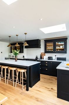 a large kitchen with black cabinets and white counter tops, wooden flooring and bar stools