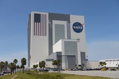 the space shuttle building with an american flag on it's side and palm trees in front