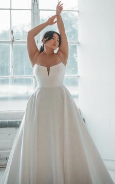 a woman in a white wedding dress is posing for the camera with her hands behind her head