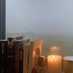 candles and books sit on a window sill in front of a foggy sky