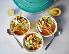 three bowls of soup with tortilla chips and avocado on the side