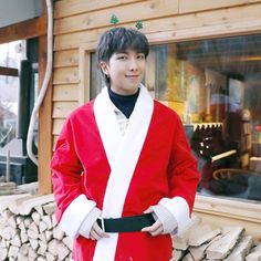 a man in a red and white robe standing next to a pile of logs